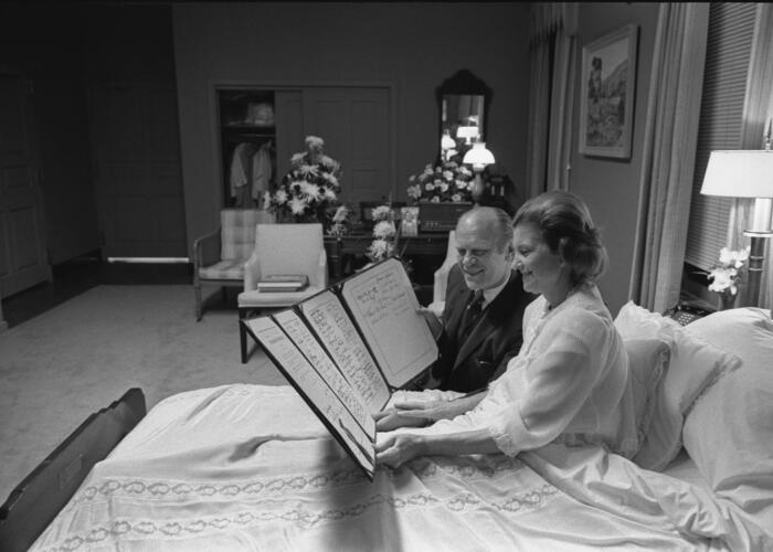Black and white photograph of man and woman in hospital room reading a large folio.