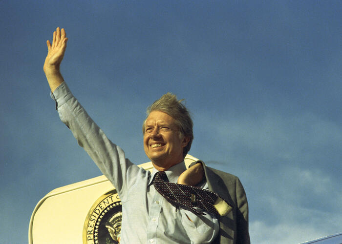 President waving at door of Air Force One with blue sky in background.
