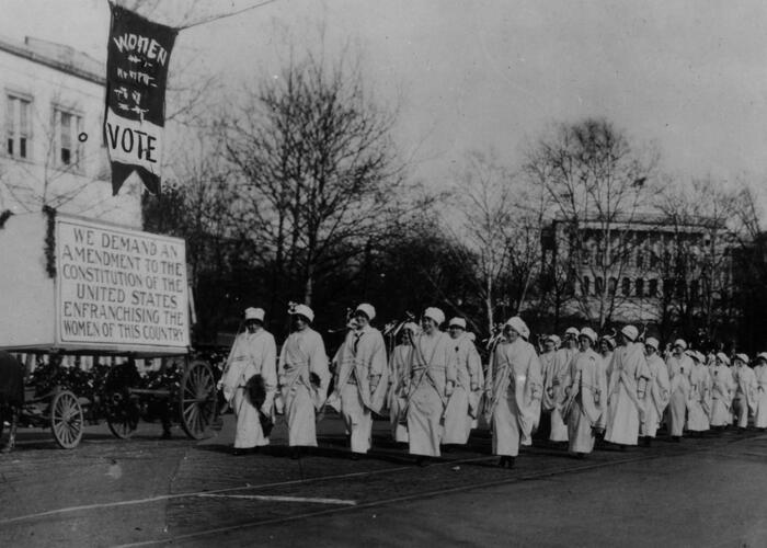Black and white image of women marching in suffragette parade on the street in  Washington, DC
