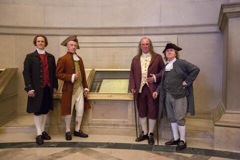 Four men portraying historical figures standing near Declaration of Independence