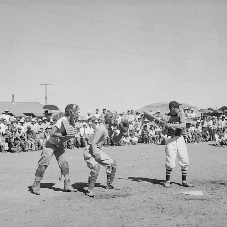 Black and white image of three men playing baseball with a crowd behind.