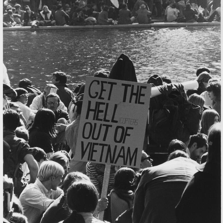 Black and white photograph of group of protestors with sign sitting around water