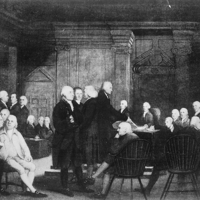 Black and white image of men sitting and standing around in a room