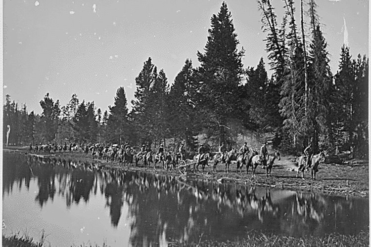 Black and white photograph of a group of men on horseback in front of a body of water.