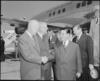Black and white photograph of men greeting in front of an airplane