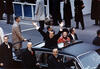 Color image of president waving from motorcade surrounded by secret service agents