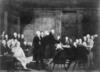 Black and white image of men sitting and standing around in a room