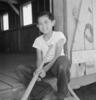 Black and white photograph of young boy sitting in a doorway holding a baseball bat.