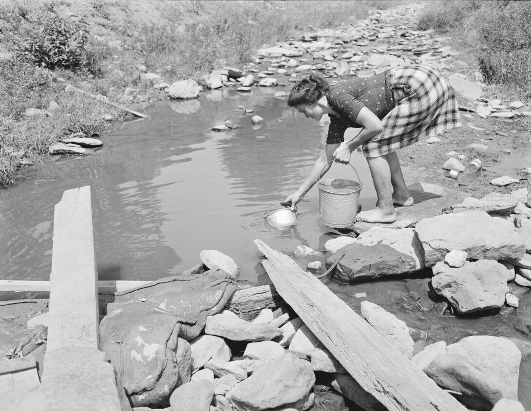 Woman getting wash water from dirty stream.