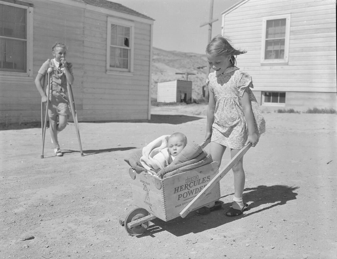 Girls playing in front of house with homemade baby buggy