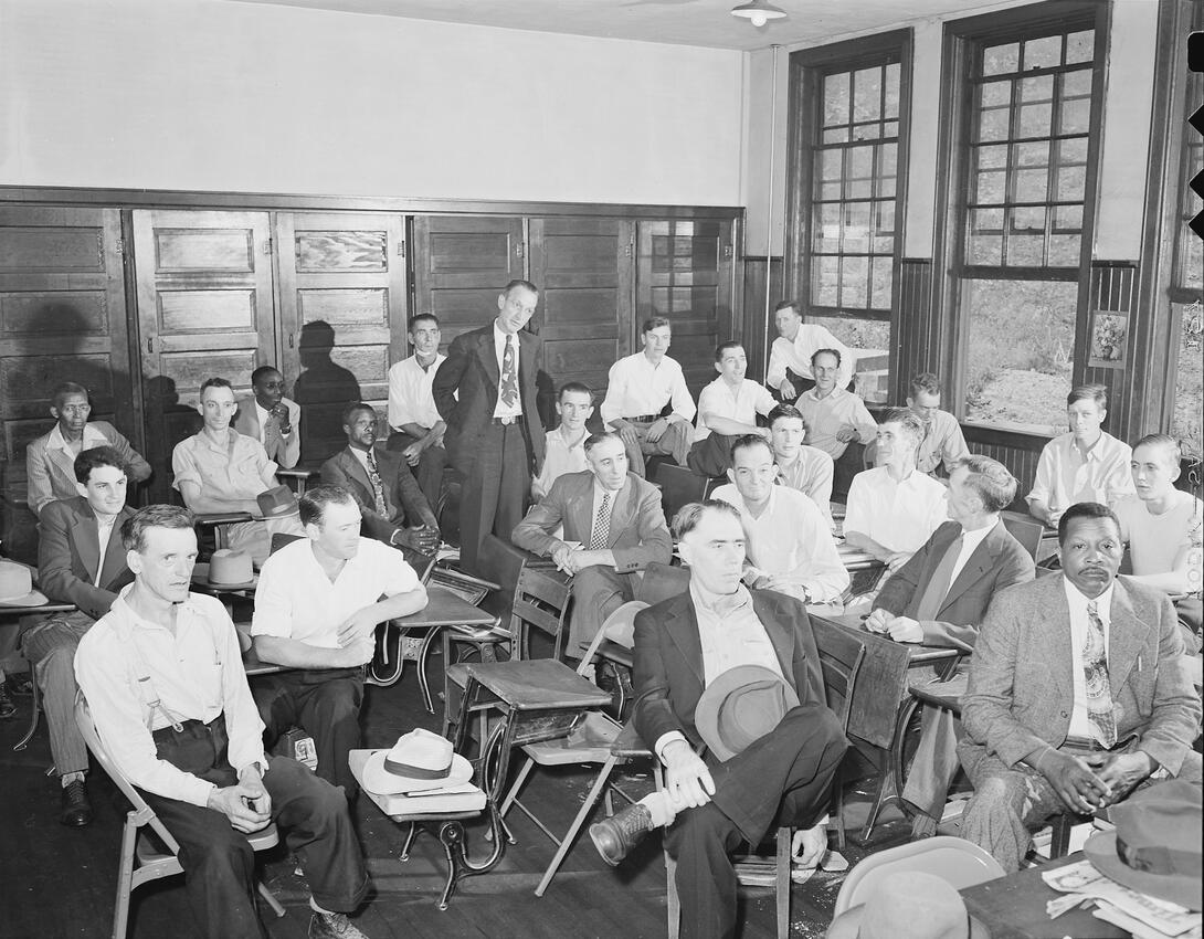 Group of men at meeting in schoolhouse.