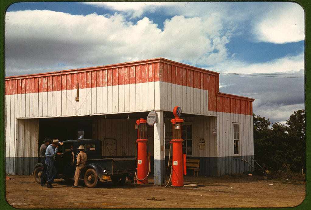 Men standing by a truck at a filling station.