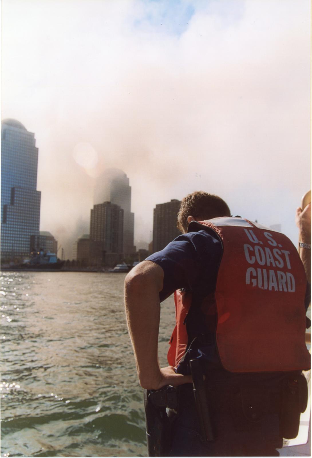 A member of the U.S. Coast Guard looks down with smoke in the distance following the attacks on September 11, 2001