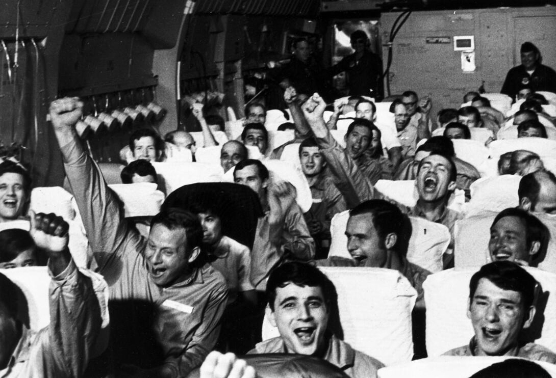 Black and white photograph of soldiers on a plane celebrating with smiles and raised fists