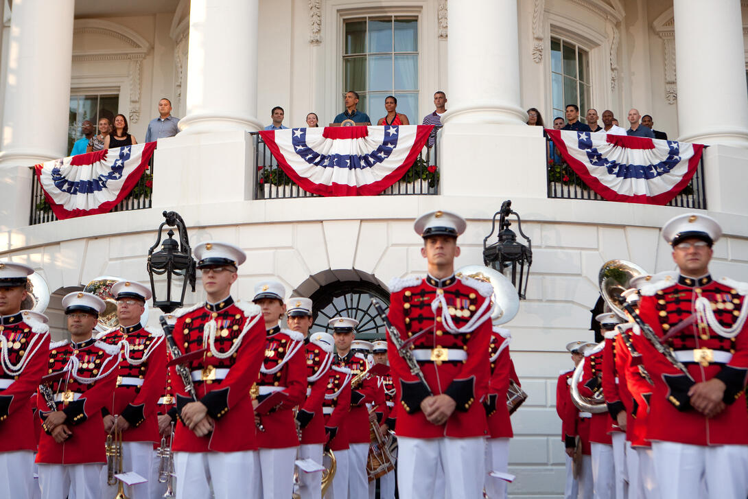 President and First Lady standing on White House balcony with soldiers standing below
