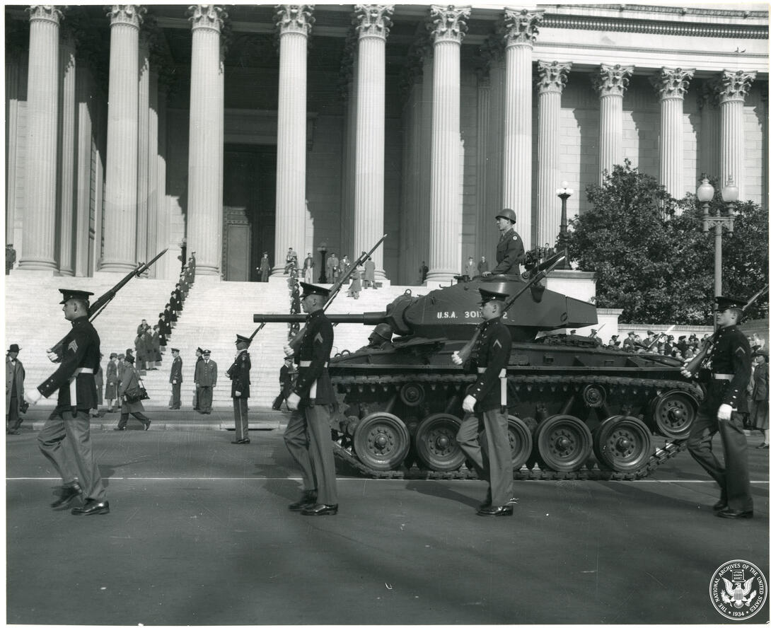 Black and white photograph of soldiers marching with a tank in front of the National Archives building