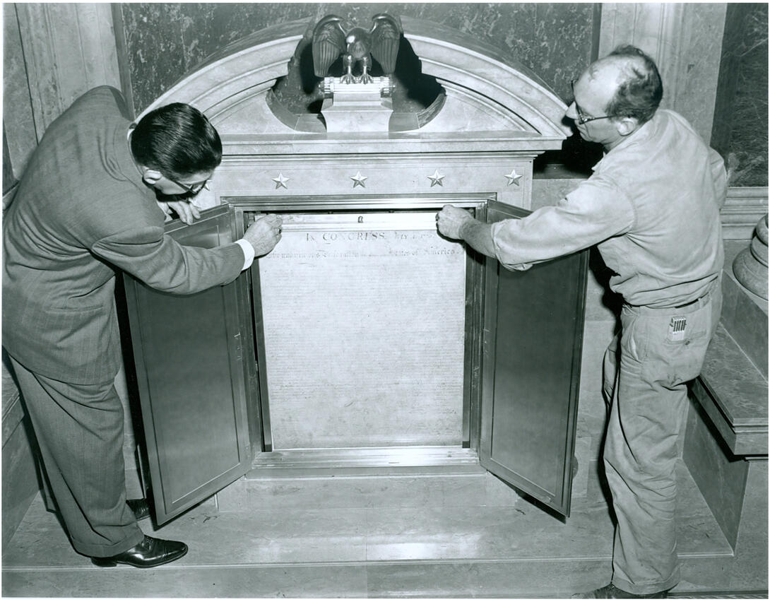 Two men placing document inside of exhibit case