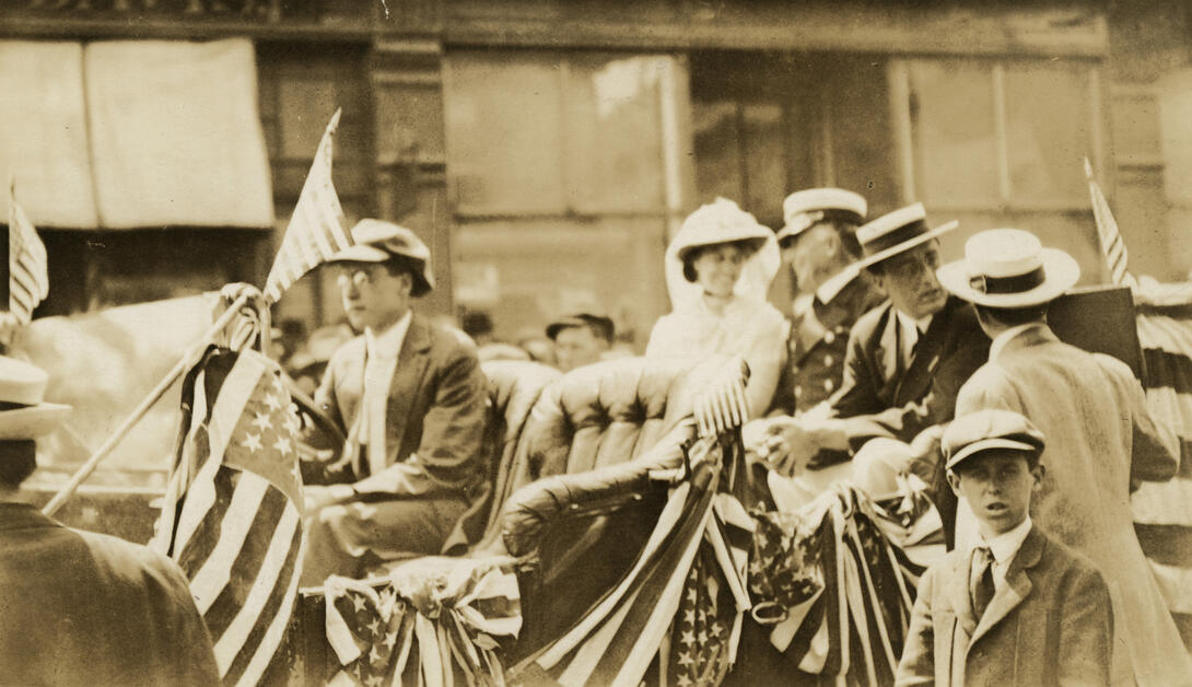 Men, women, and children with a car festooned with flags and bunting