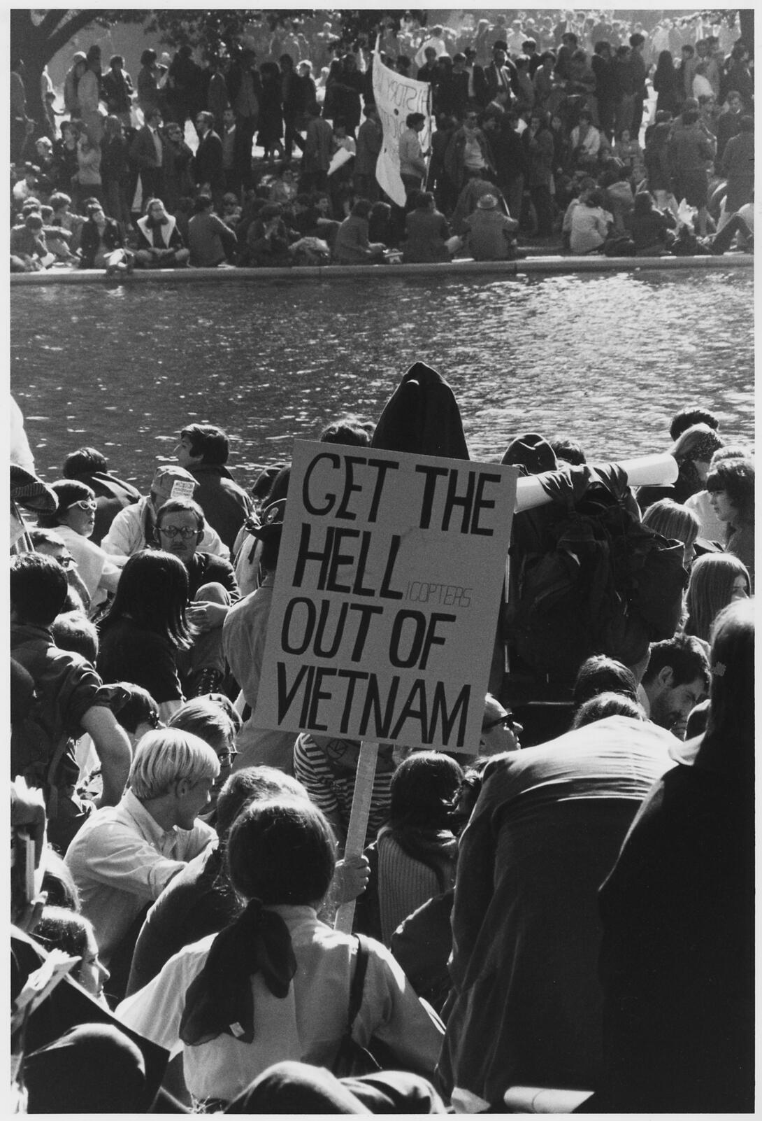 Black and white photograph of group of protestors with sign sitting around water