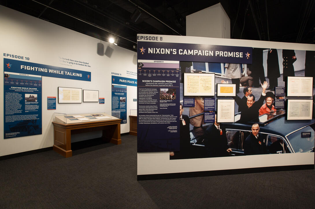 Color photograph of exhibit gallery with image of exhibit case and president in limousine