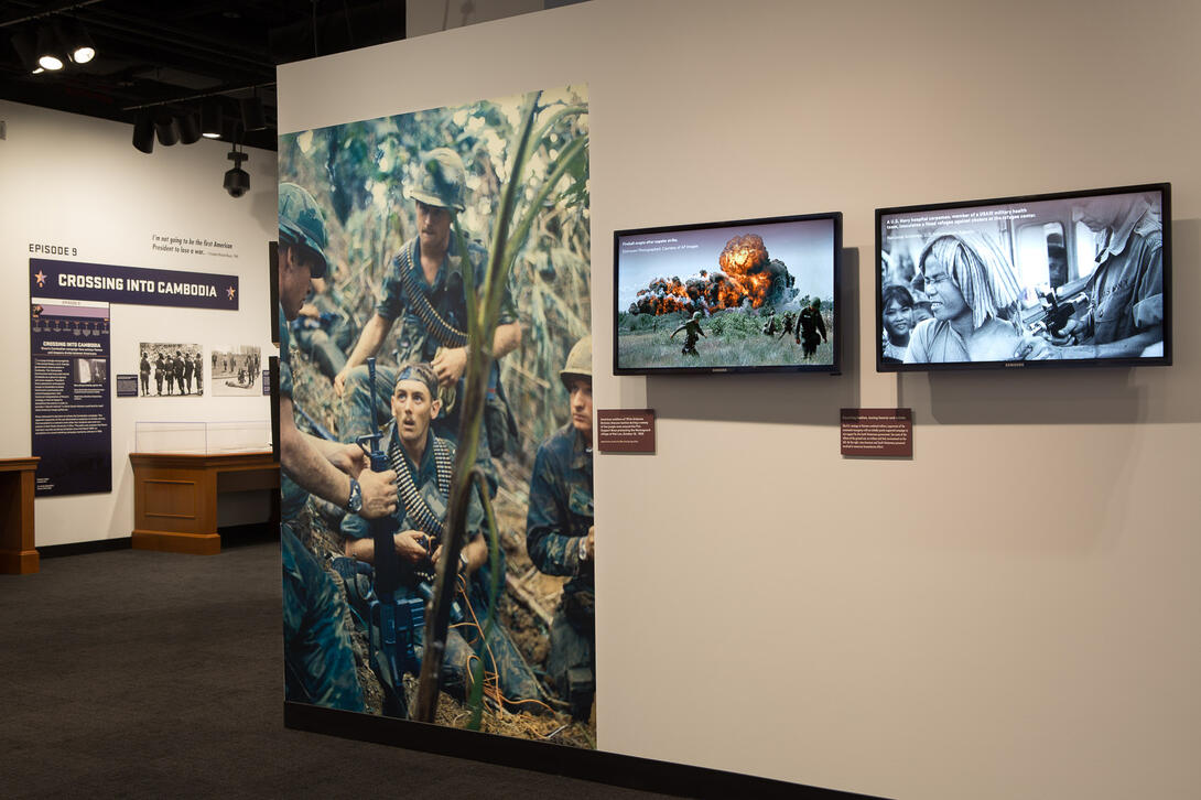 Color photograph of exhibit gallery with case, images, and video screens