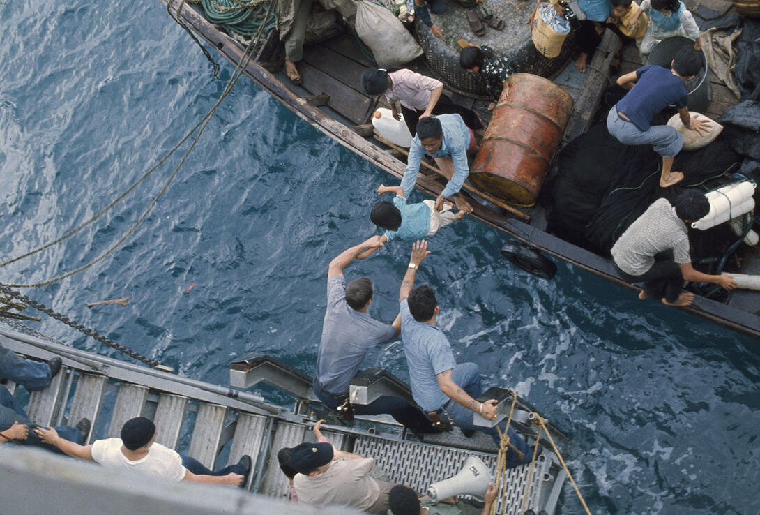 Color photograph of crewmen rescuing child from a refugee boat in sea